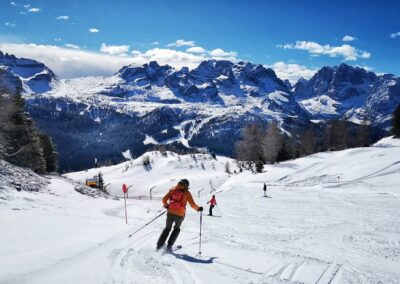Skiers descending a sunny slope in Val di Sole with panoramic views of the Brenta Dolomites