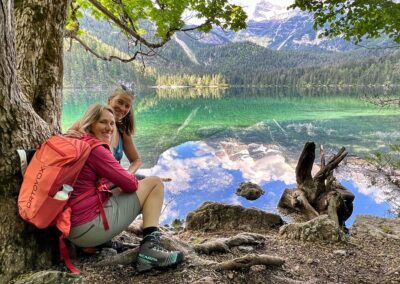 Two hikers relaxing beside a crystal-clear alpine lake Lago Di Tovel surrounded by forests and mountains
