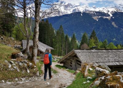Hiker walking past traditional mountain huts with views of the snow-capped mountains in the Adamello Brenta Nature Park