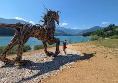 Large wooden sculpture beside a blue mountain lake in Val di Sole, Trentino, Italy